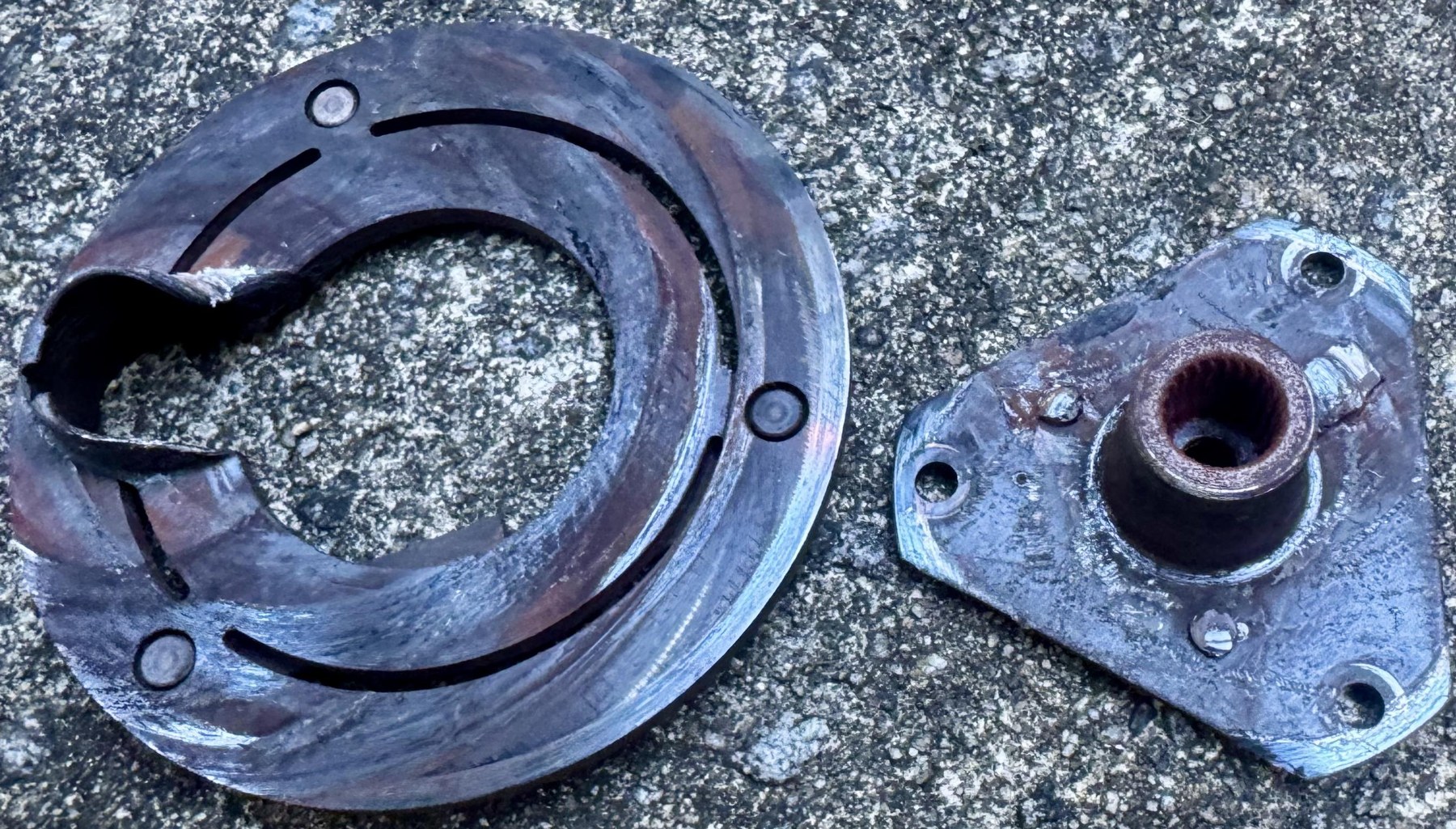Removed Corvette A/C clutch face with a large heat-damaged opening beside its separated hub.